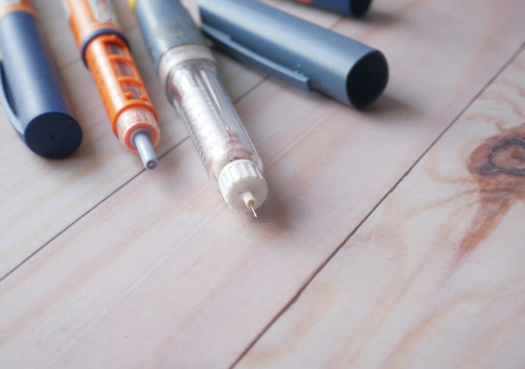 Mehrere Abnehmspritzen Pens auf Holztisch – Kosten und Krankenkassen-Erstattung von GLP-1-Medikamenten wie Ozempic, Wegovy oder Mounjaro