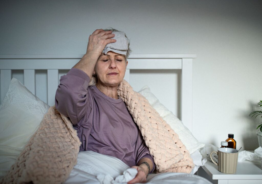 Frau liegt krank im Bett mit Handtuch auf der Stirn – mögliche Nebenwirkungen der Abnehmspritze wie Übelkeit oder Unwohlsein